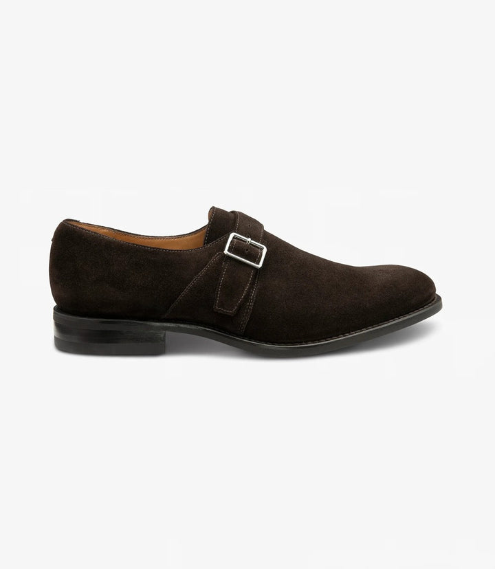 The dark brown suede Loake 357 Oxford is shown from the side, highlighting its smooth suede texture and the classic single monk strap. The Goodyear welted rubber sole is visible, adding to the shoe's durability and structure.