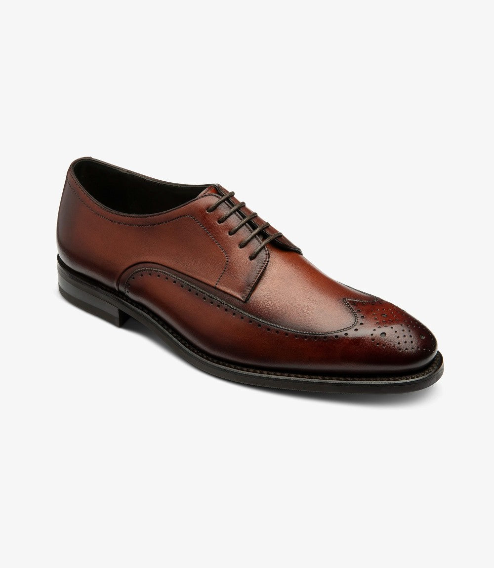 Captured from a dynamic angle, the shoe reveals its sophisticated design elements, including the intricate punched brogue accents that add character. The soft curvature of the Derby silhouette complements the comfortable fit, with the leather lining visible through the slightly opened flap, hinting at the premium materials used.