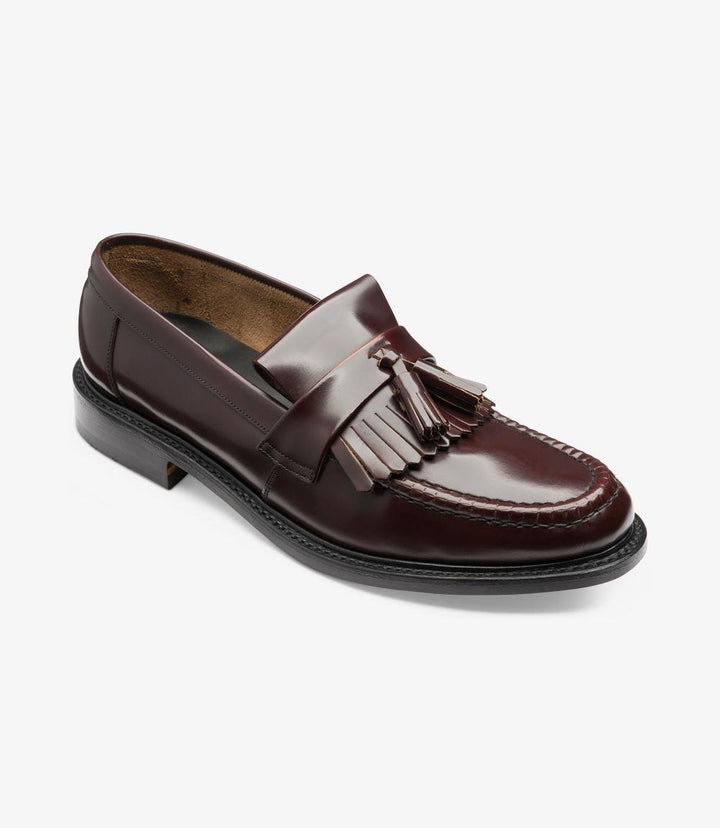 An angled shot highlighting the sophisticated silhouette of the loafer, capturing the shine of the polished leather and the classic tassel detailing. The comfort of the leather insole and the structure of the narrow fit are evident from this perspective.