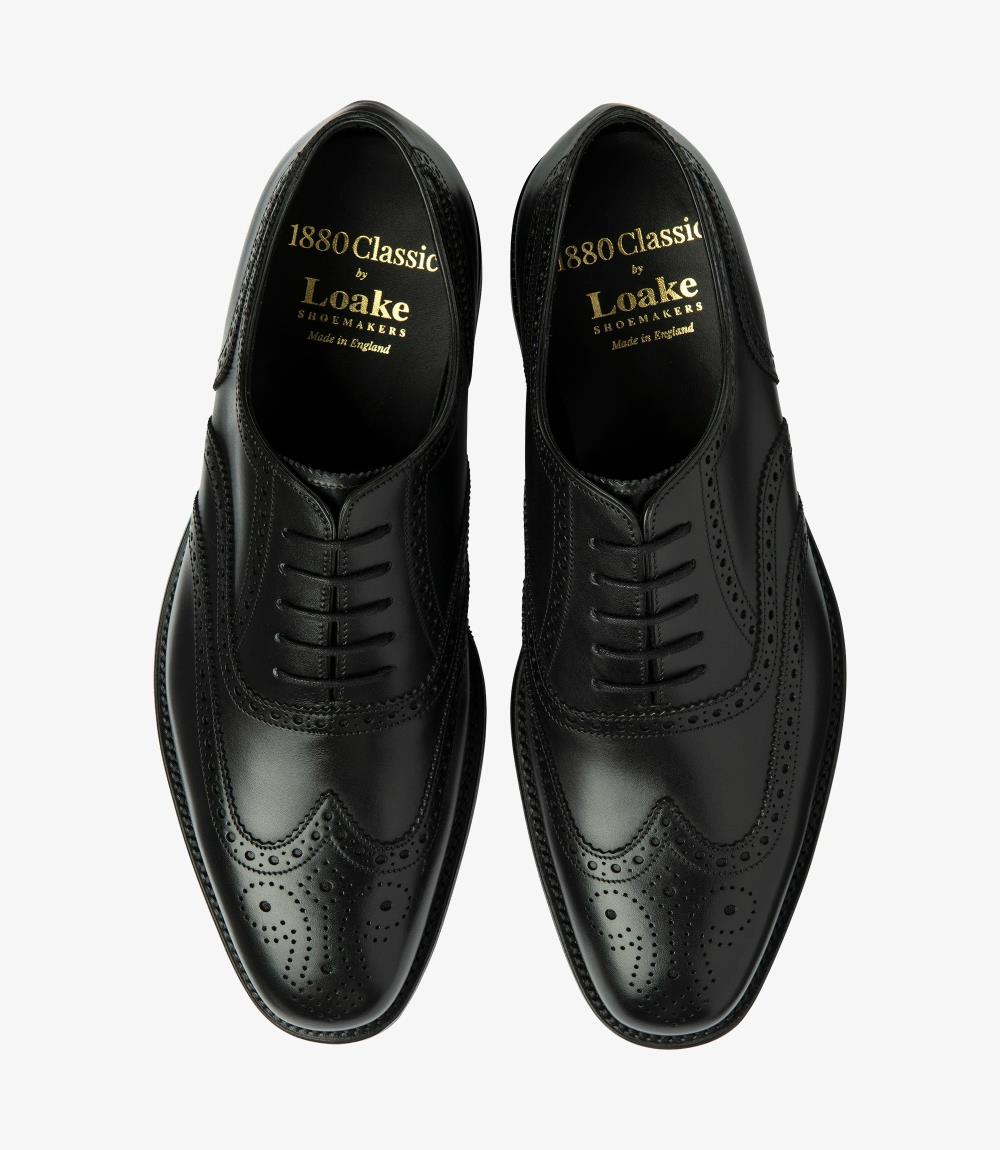 A top-down view of two Loake Buckingham Black Oxford Brogues neatly arranged side by side. The polished finish of the black burnished calf leather reflects a luxurious sheen, while the full brogue design, complete with intricate detailing, creates a stunning visual impact. This perspective showcases the symmetrical elegance of the shoes, highlighting their craftsmanship and classic style.