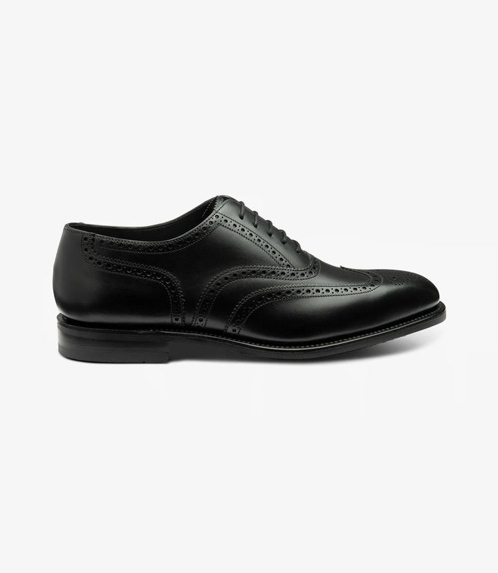 A detailed side view of the Loake Buckingham Black Oxford Brogue showcases its elegant silhouette. The premium black burnished calf leather gleams subtly in the light, highlighting the intricate brogue detailing and perforations along the eyelets and toe cap. The Goodyear welted rubber sole provides stability and durability, enhancing the shoe's refined appearance.