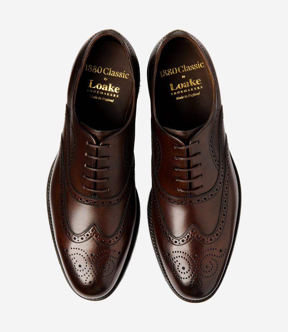 A shot of both shoes side-by-side underscores the symmetry and craftsmanship of the Loake Castlegate Scorched Walnut Oxfords. The intricate brogue detailing and the elegant scorched walnut color are prominent, with the shadow rubber soles and fully leather-lined interiors contributing to a cohesive and refined appearance. This view highlights the classic design and superior build quality of the shoes.