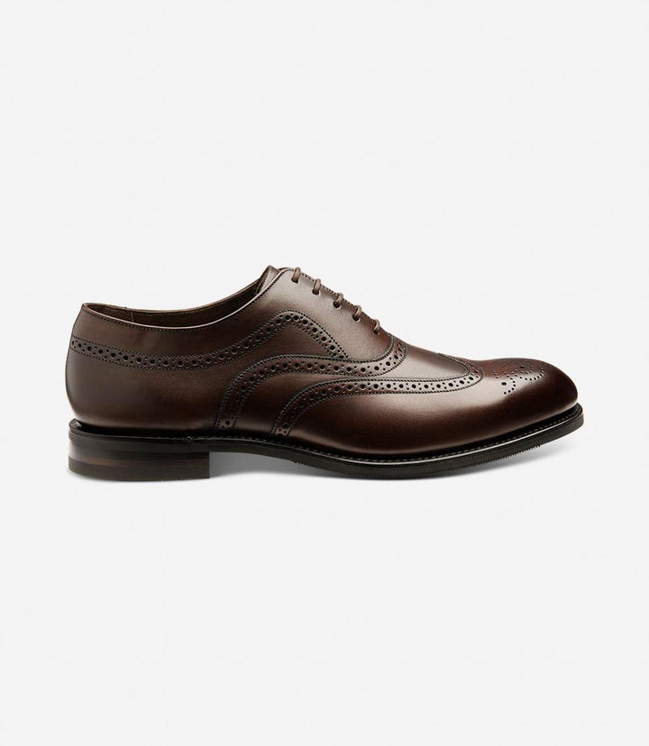 The Loake Castlegate Scorched Walnut Oxford Brogue is captured from a classic side perspective, highlighting its sleek silhouette. The rich, scorched walnut calf leather gleams with a luxurious finish, while the intricate brogue detailing along the toe and sides adds a touch of timeless elegance. The shadow rubber soles, designed for durability and superior grip, are subtly visible.