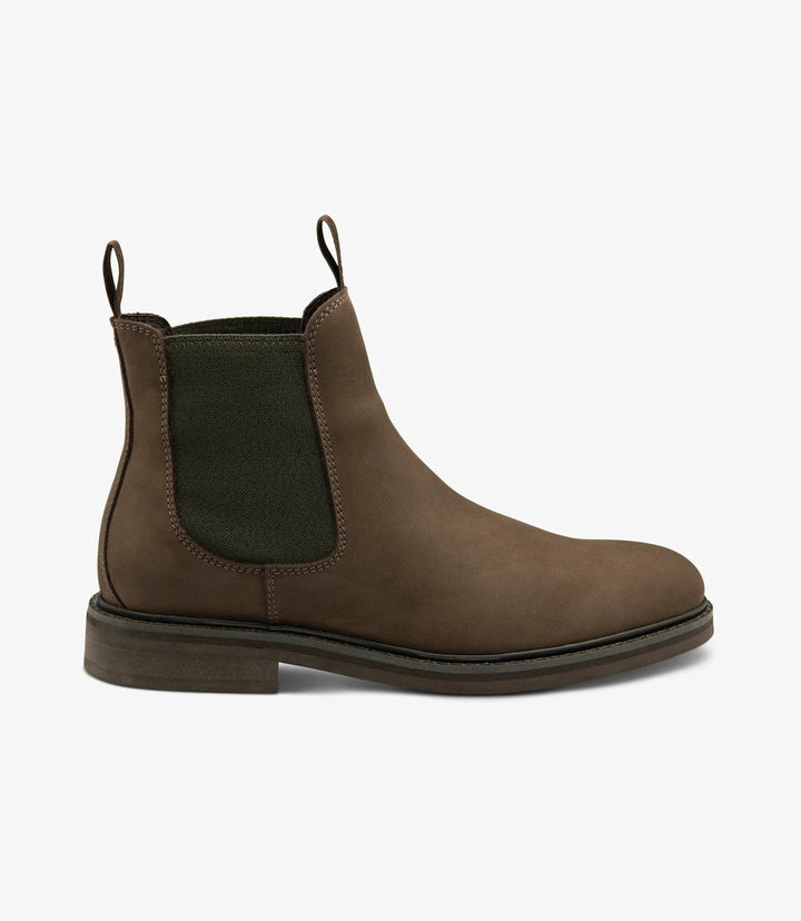 The image captures the side profile of the Loake Ducksworth Brown Chelsea Boot, showcasing its sleek silhouette. The oiled nubuck leather has a rich, warm brown hue that glistens subtly in the light. The elastic side panels blend seamlessly into the design, allowing for easy slip-on access. The cemented rubber sole is visible at the bottom, emphasizing durability and grip.