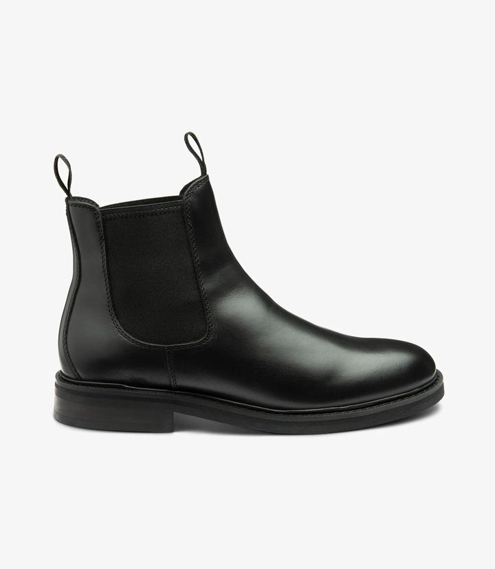 The side view of the Loake Ducksworth Black Chelsea Boot showcases its sleek, minimalist silhouette crafted from premium waxy leather. The smooth leather gleams softly in the light, while the subtle stitch detailing adds a refined touch. The boot features a classic elasticated panel for easy slip-on wear, seamlessly integrating with the boot's streamlined design. The cemented rubber sole is visible, providing both durability and grip, enhancing the overall modern aesthetic.