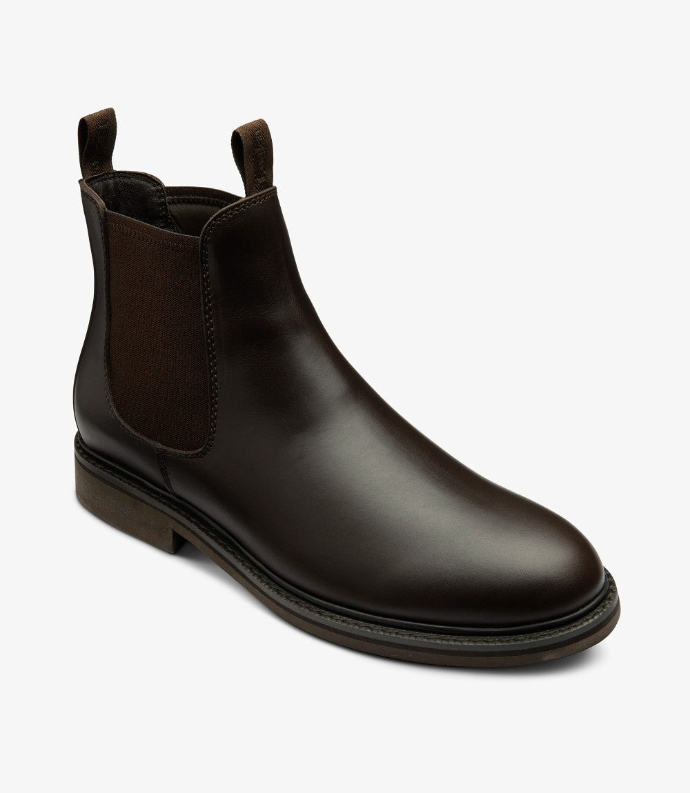 In this angle, the Chelsea boot is presented slightly turned to emphasize its profile. The curvature of the boot is accentuated, showcasing the comfortable fit around the ankle. The cemented rubber sole is clearly visible, demonstrating its durability and grip, while the intricate detailing of the waxy leather adds depth to the overall appearance.