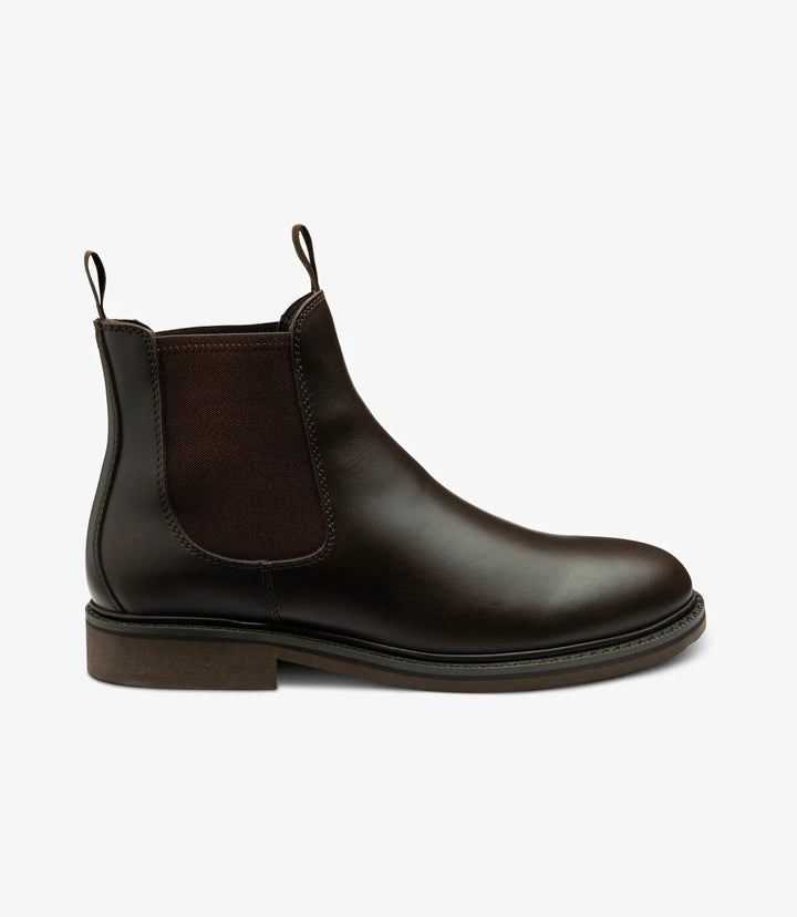 This image showcases the Loake Ducksworth Dark Brown Chelsea Boot from the side. The smooth, waxy leather shines under the light, highlighting the rich dark brown hue. The elastic side panels are visible, offering both style and functionality. The clean silhouette and sleek design exemplify classic Chelsea boot aesthetics.