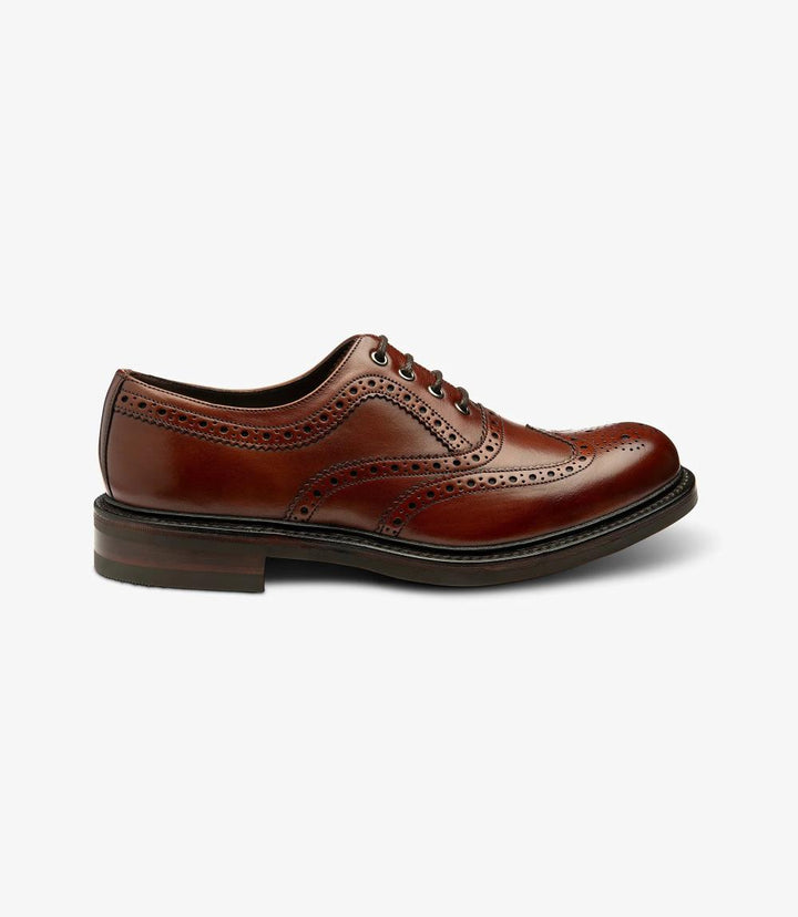 The photo captures the elegant silhouette of the Loake Edward Mahogany Oxford Brogue from the side. The rich mahogany hand-painted calf leather gleams under soft lighting, showcasing its luxurious texture. The intricate brogue detailing along the toe and sides adds a classic touch, while the Goodyear welted rubber sole is visible, indicating durability and quality craftsmanship.