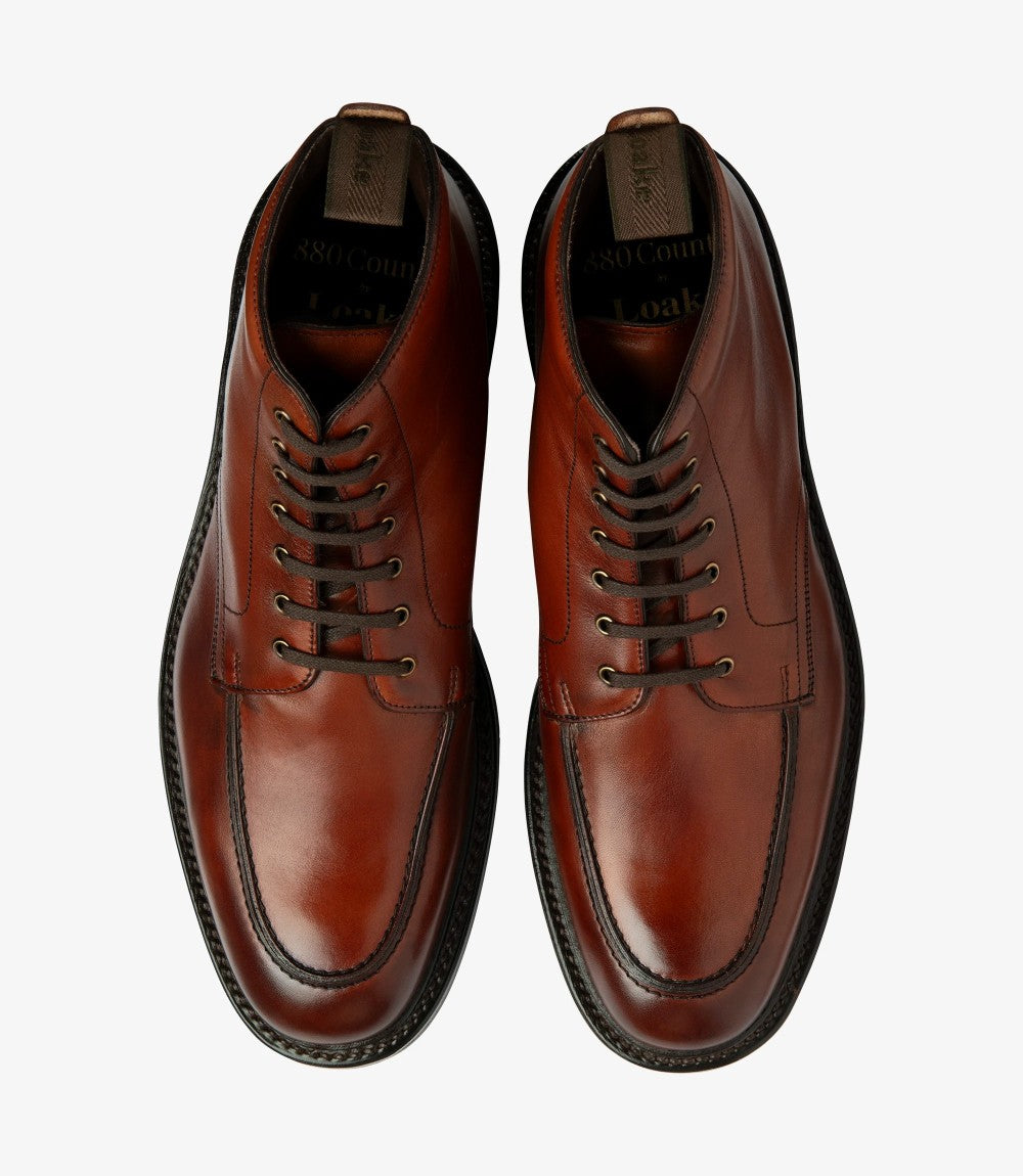 The overhead shot features both Loake Gisbourne Derby Boots side by side, allowing a clear view of their matching mahogany hue and sleek design. The fully leather-lined interior is subtly visible, suggesting comfort, while the textured rubber soles provide contrast, ensuring excellent grip.