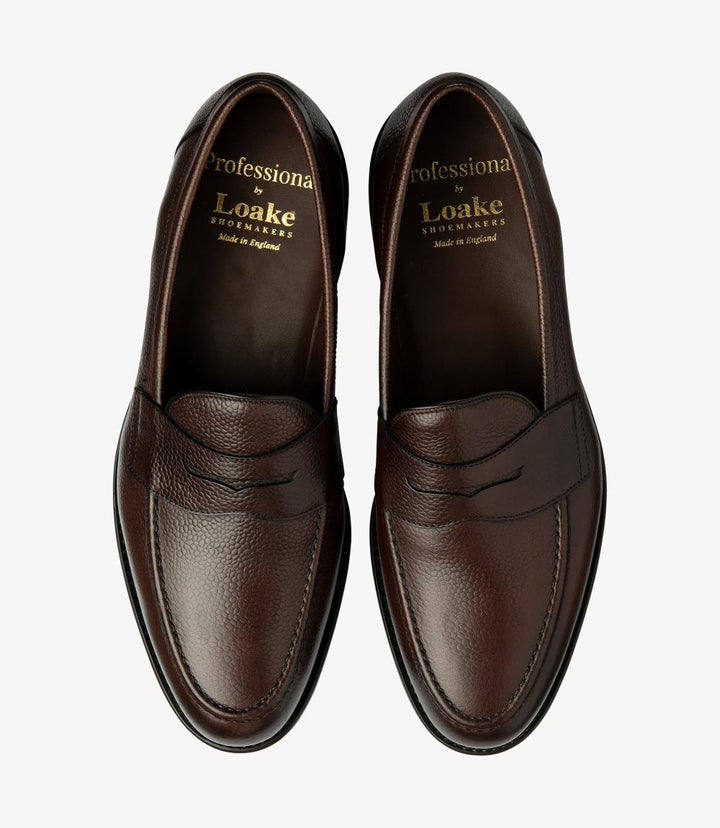 The overhead view of the Imperial Grain Dark Brown Loafers presents both shoes side by side, offering a comprehensive look at their sophisticated design. The polished burnished leather surfaces reflect a deep, inviting brown tone, while the classic penny loafer style is accentuated by the distinctive cutout. The cushioned insoles are slightly visible, hinting at the comfort that awaits with each step. This view captures the elegant symmetry and refined appeal of the loafers.