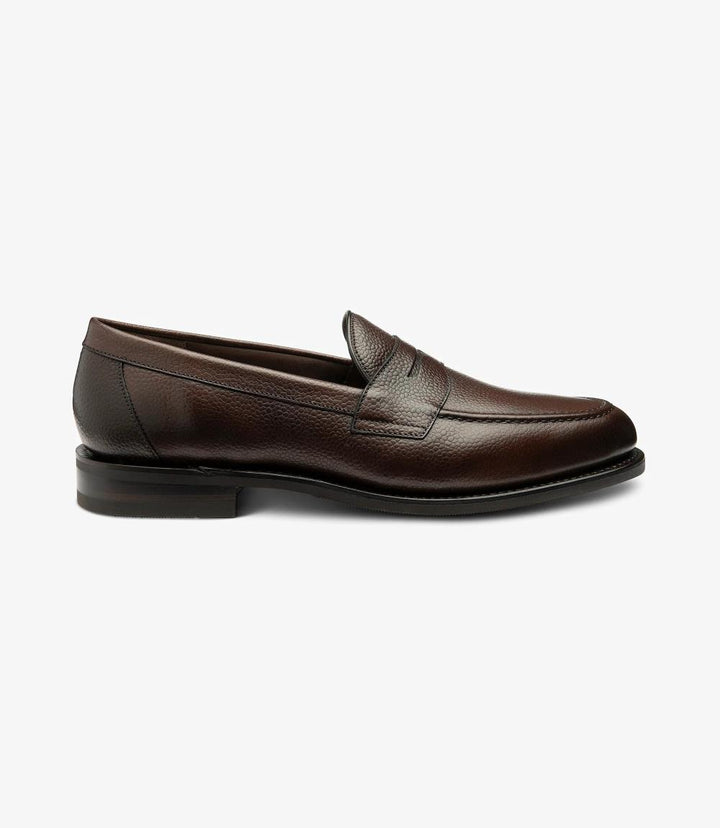 The side view of the Imperial Grain Dark Brown Loafer highlights its elegant silhouette and rich burnished grain calf leather. The polished surface catches the light, showcasing the deep brown color and the shoe’s sophisticated finish. The classic apron design features refined stitching, while the Goodyear welted shadow rubber sole provides a glimpse of the durable construction. This angle captures the timeless essence of the loafer, emphasizing its versatility and style.