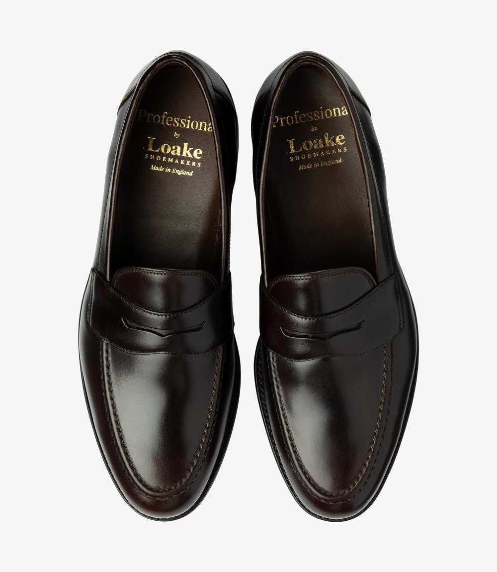 The overhead view of the Imperial Dark Brown Loafers presents both shoes side by side, offering a comprehensive look at their sophisticated design. The polished waxy leather surfaces reflect a rich, inviting tone, while the classic penny loafer style is accentuated by the distinct cutout. The cushioned insoles are slightly visible, hinting at the comfort that awaits. This view captures the elegant symmetry of the loafers, showcasing their versatility and timeless appeal.