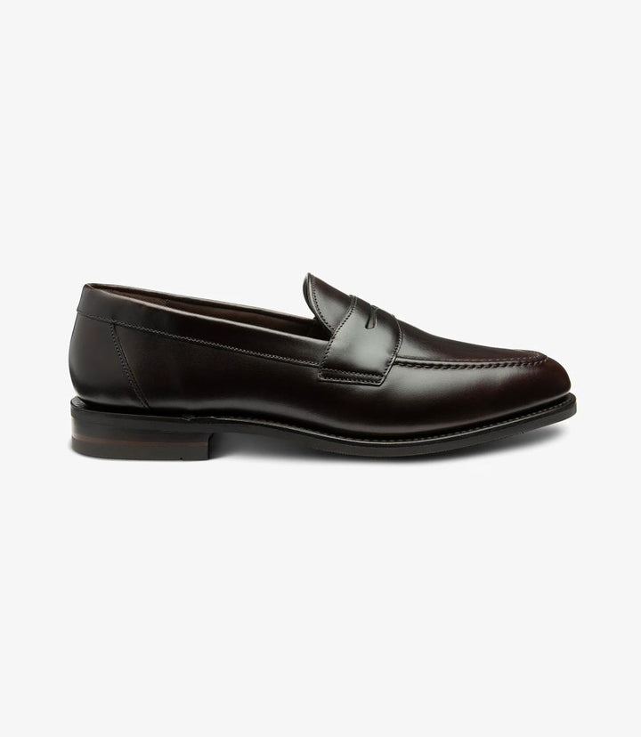 The side view of the Imperial Dark Brown Loafer showcases its refined silhouette, highlighting the sleek lines and elegant design. The rich waxy leather glistens subtly, reflecting light and accentuating its deep brown hue. The classic apron design is complemented by precise stitching that adds a touch of sophistication. The Goodyear welted shadow rubber sole is visible, underscoring the shoe's durability and craftsmanship while enhancing its overall profile. 