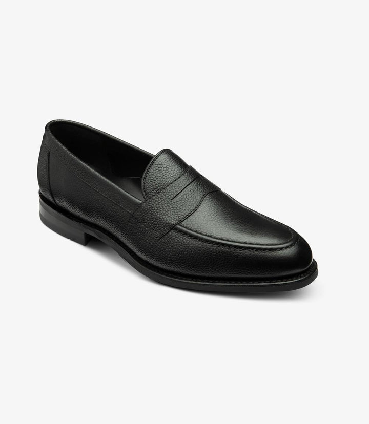 From this angle, the Imperial Grain Black Loafer reveals its stylish contours and expertly crafted shape. The smooth grain calf leather curves elegantly from the toe to the heel, complemented by the classic apron design. The subtle sheen of the leather catches the light, while the shadow rubber sole provides a glimpse of the shoe's robust construction. 