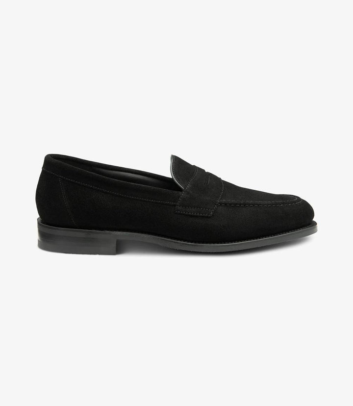 The side view of the Imperial Suede Black Loafer showcases its elegant silhouette, highlighting the soft texture of the premium black suede. The smooth lines flow seamlessly from the rounded toe to the heel, while the classic apron design features refined stitching that adds sophistication. The Goodyear welted shadow rubber sole peeks out from below, emphasizing both durability and style. This perspective captures the loafer's timeless appeal, making it a versatile choice for various occasions.