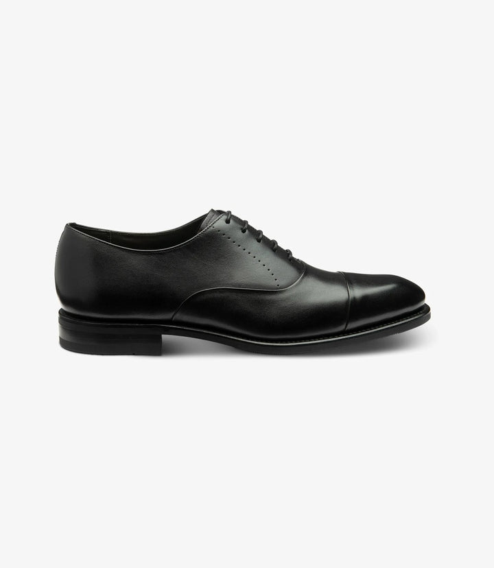 This image captures the sleek profile of the Loake Phoenix Black Oxford Toe Cap. The premium black calf leather gleams under the light, highlighting the elegant toe-cap design. The Goodyear welted shadow rubber sole is clearly visible, providing a sturdy base that enhances the shoe's classic silhouette.