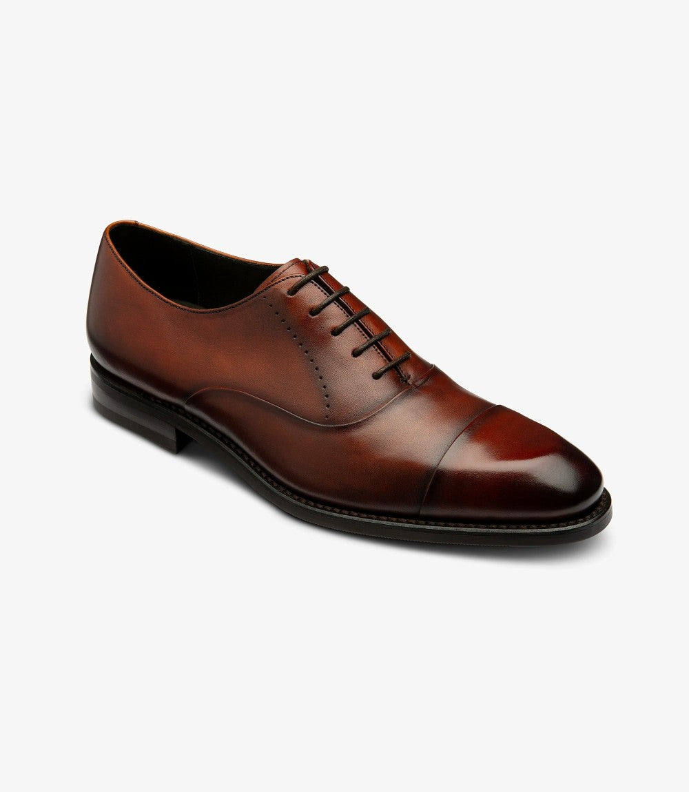 An angled view of the shoe emphasizes the smooth lines and sophisticated shape of the Loake Phoenix. The contrast between the polished scotch calf leather and the Goodyear welted shadow rubber sole is evident, illustrating the shoe’s craftsmanship. This perspective also reveals the well-defined toe cap, enhancing its stylish appeal.