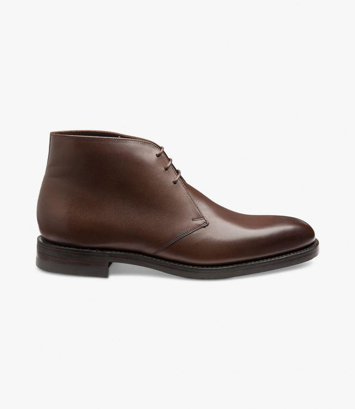 The side of the Pimlico-DIS Dark Brown Derby Boot reveals its sleek, burnished calf leather with a rich dark brown hue. The Goodyear Welted Danite rubber sole is visible, showcasing its durability and grip. The chukka boot design features clean lines and a refined silhouette, perfect for versatile styling.