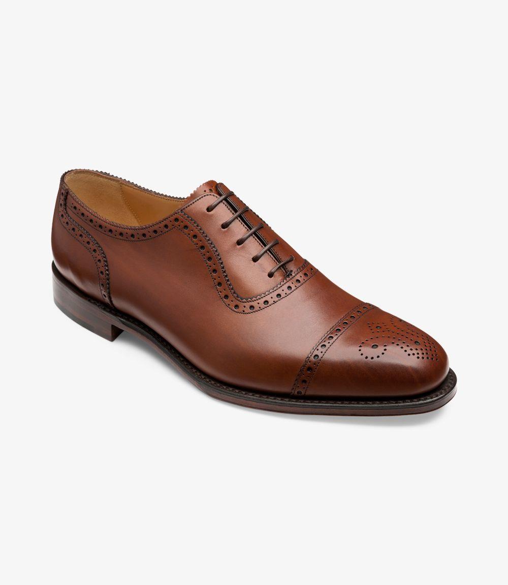 This angled shot captures the Loake Strand-DIS Oxford from a dynamic perspective, emphasizing the semi brogue's detailed craftsmanship. The burnished leather appears more textured, and the decorative perforations on the toe cap are prominent. The Goodyear welt construction is visible, demonstrating the shoe’s superior build quality. The angle also showcases the luxurious leather lining and the polished finish.