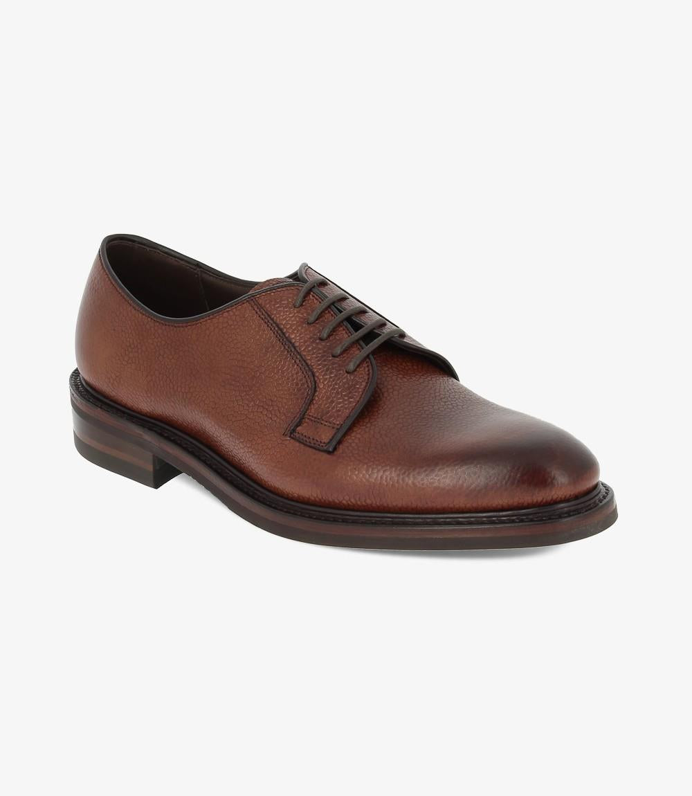 At an angle, the shoe’s textured leather finish and classic derby shape are on full display, showing off the smooth curves of the toe and the slightly raised heel. The studded rubber sole adds a hint of ruggedness, balancing sophistication with functionality.