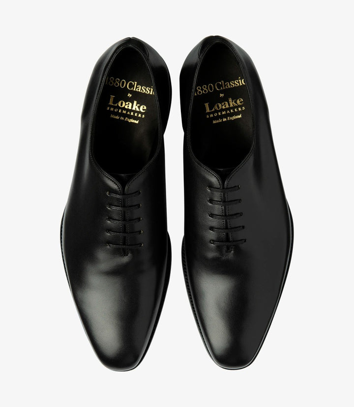 Viewed from above, the Loake Wholebury Black Oxford Shoes display their symmetrical design and classic lacing system. The black leather is smooth and refined, showcasing the craftsmanship that goes into each pair. The eyelets are neatly aligned, and the laces are securely tied, creating a polished appearance. The toe box is slightly rounded, allowing for both style and comfort, making these shoes ideal for long wear.