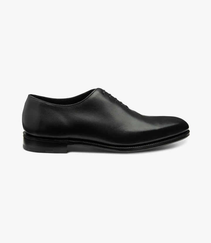 The side view of the Loake Wholebury Black Oxford Shoes showcases their elegant silhouette, featuring a sleek, polished black leather upper. The clean lines and understated design emphasize the classic oxford style. The Goodyear welt construction is visible at the junction of the upper and sole, highlighting the craftsmanship. The lacing system, with its five eyelets, adds a refined touch, while the leather sole extends seamlessly from the upper, providing a sophisticated look.