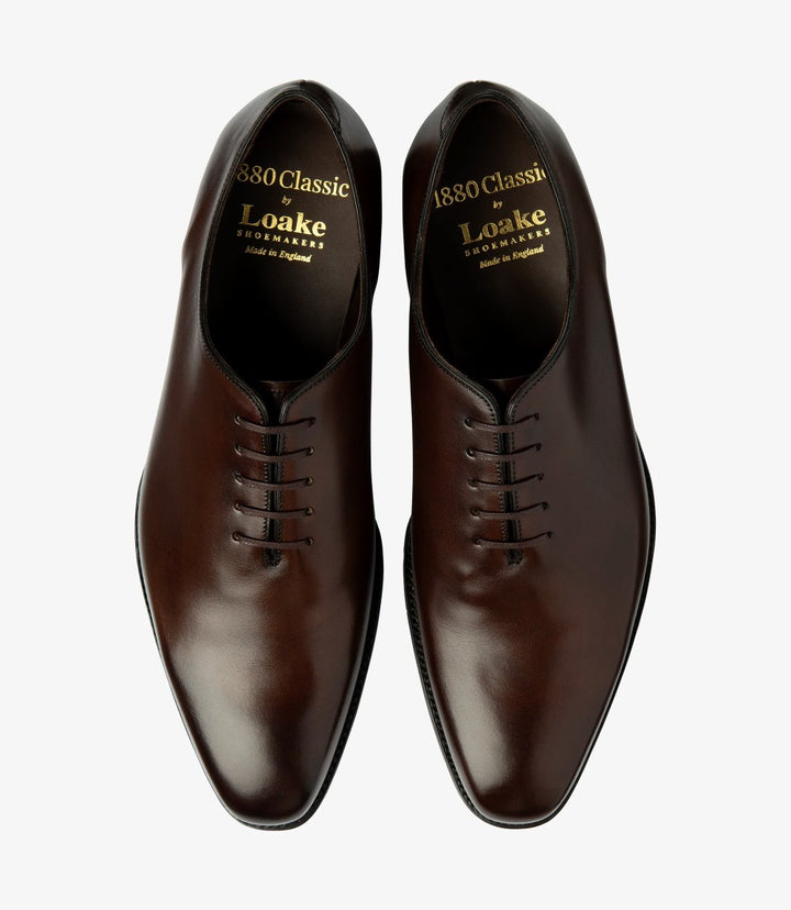 The top view of the Loake Wholebury Dark Brown Oxford Shoes presents a symmetrical and polished appearance. The smooth leather upper is complemented by the well-structured lacing system, with neatly aligned eyelets leading to the rounded toe. The clean lines of the shoe emphasize its classic oxford style, while the fully leather-lined interior is suggested by the quality of the materials. 