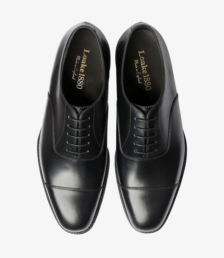 The overhead shot of the Aldwych Oxford shoes reveals the intricate details of the shoe's design. The classic toe cap sits prominently at the front, while the symmetrical lacing system enhances the shoe's elegance. The smooth black leather surface reflects the light, showcasing the impeccable craftsmanship and quality of materials used in the construction.