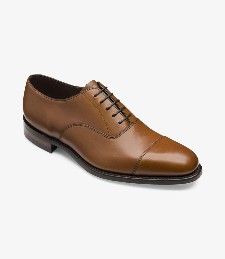 This photo presents the Aldwych Oxford from a dynamic angle, capturing the shoe's depth and details. The slight curvature of the shoe is accentuated, showcasing the contours that hug the foot. The glossy mahogany leather reflects light beautifully, while the toe-cap adds a touch of classic elegance. The image emphasizes the sturdy yet refined silhouette, making it clear that these shoes are designed for both style and comfort.