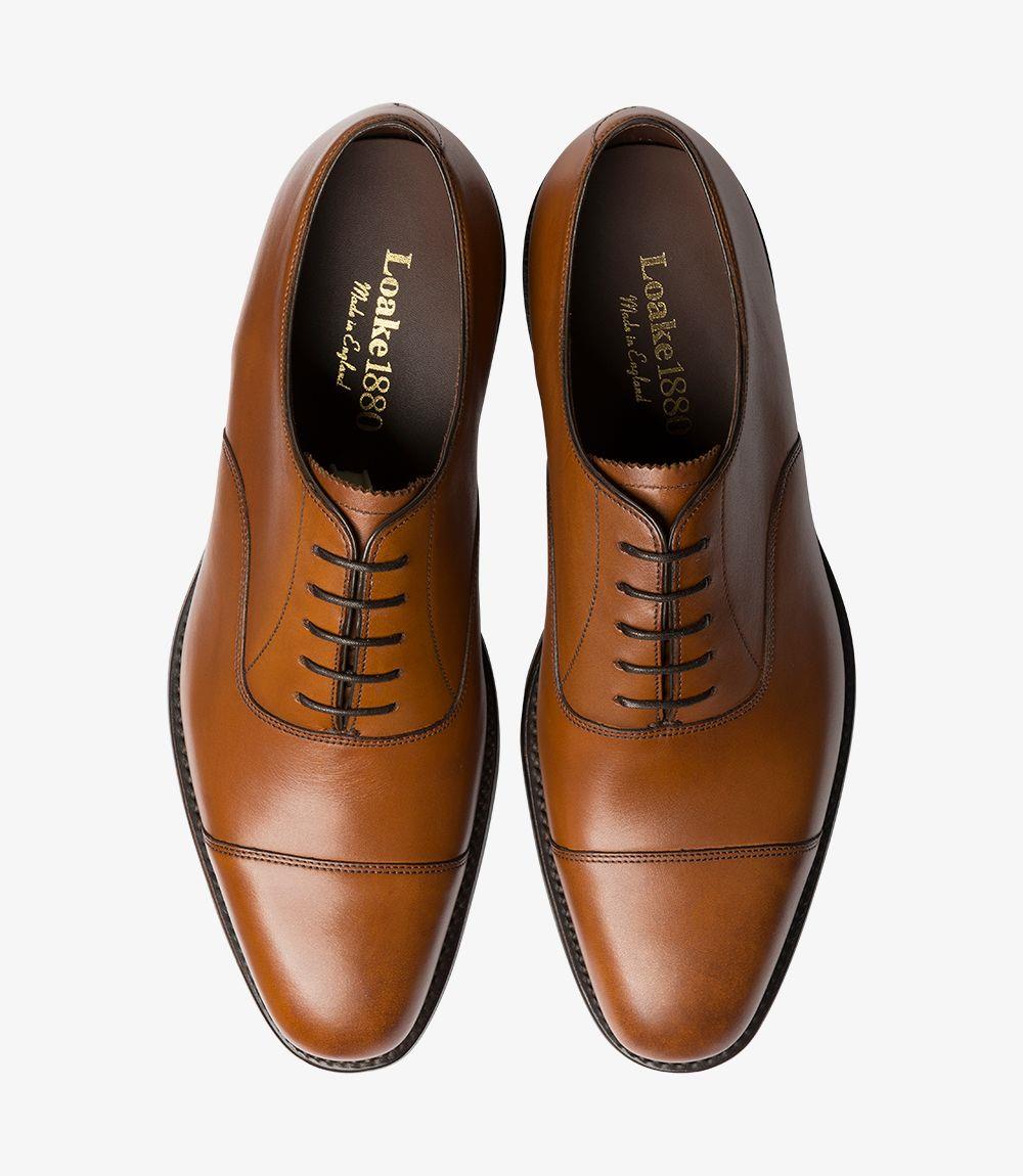 The overhead view reveals the complete outline of the Aldwych Oxford shoes, showcasing the symmetrical toe-cap design. The polished surface of the mahogany leather gleams under the light, while the smooth lines converge towards the sleek laces. This angle highlights the shoe's elegant profile and craftsmanship, giving a clear view of the leather texture and quality construction.