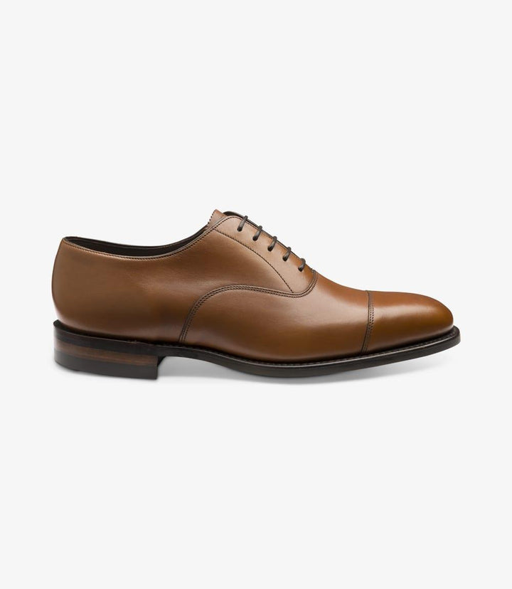 The image showcases the Aldwych Mahogany Oxford Toe-Cap shoe from the side. The smooth mahogany leather exhibits a rich, warm hue, highlighting the shoe's elegant profile. The toe-cap design adds sophistication, while the sleek lines lead to a polished finish. The Goodyear welted construction is subtly visible, indicating quality craftsmanship.