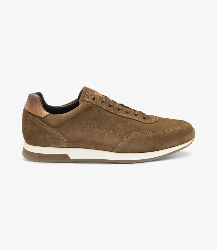 The side view of the Loake Bannister Tan Suede Trainer showcases its sleek silhouette, featuring a rich tan suede upper that adds a touch of elegance. The shoe's clean lines and understated sportswear detailing contribute to its contemporary aesthetic. The durable cemented rubber sole is slightly visible, offering a hint of the sneaker's practical design. The lace-up front, with matching tan laces, creates a harmonious look that complements the suede material.