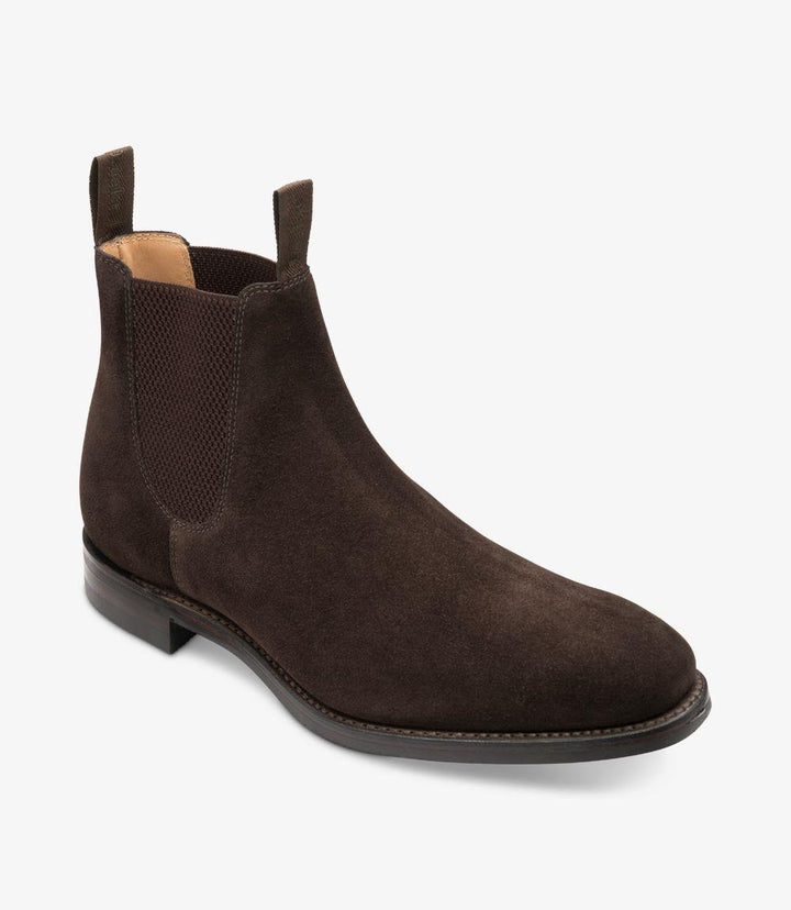 Captured at a slight angle, this photo of the Loake Chatsworth Chelsea Boot emphasizes the depth and texture of the dark brown suede. The boot's elastic side panels provide a modern twist, ensuring easy wear while maintaining a streamlined look. The rubber sole is slightly visible at the bottom, showcasing its practicality and grip, perfect for both casual and formal settings.