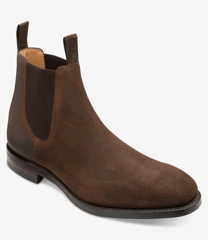 This angle reveals the boot’s elegant profile, highlighting the gently rounded toe and the sleek line that extends from the heel to the toe. The rich brown waxed suede contrasts beautifully with the dark rubber sole, which provides a modern twist on a classic Chelsea boot design. The slight curvature of the heel is visible, enhancing the overall stylish appearance.