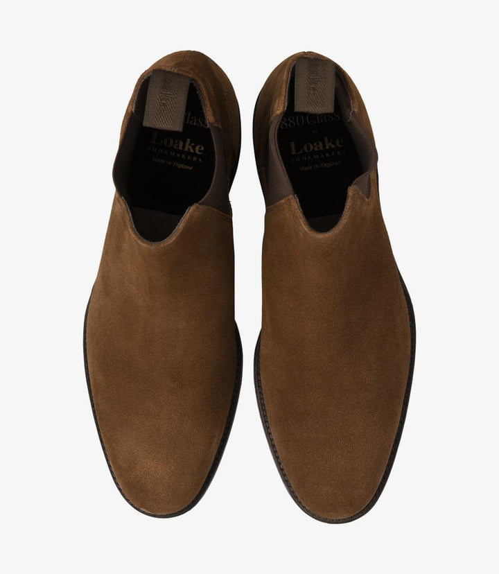 In this overhead shot, both Chelsea boots are displayed side by side, allowing for a clear view of their elegant lines and overall design. The wide elastic gussets and the smooth tobacco suede are prominent, while the rounded toe adds to the boot's classic appeal. The soft suede texture is highlighted, providing a luxurious feel, making these boots an attractive option for any outfit.