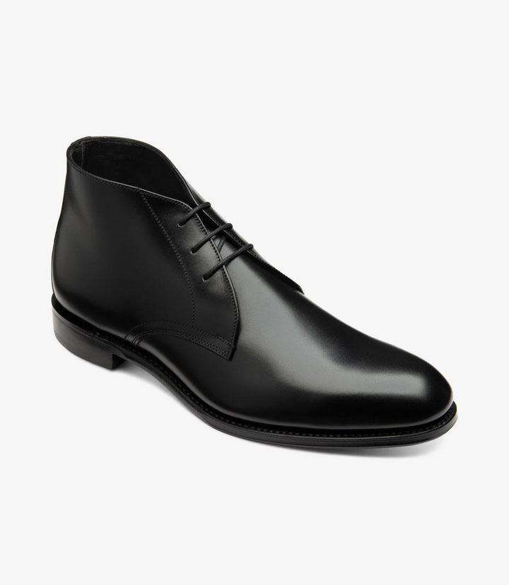 In this angled shot, the Deangate Chukka Boot is positioned to reveal both the side and the front of the shoe. This perspective highlights the elegant curve of the boot, showcasing the delicate lines of the lacing system and the soft, rounded toe. The subtle texture of the eco-tanned leather is accentuated, demonstrating the quality of the material used. The contrast between the glossy upper and the matte shadow rubber sole adds a stylish touch.