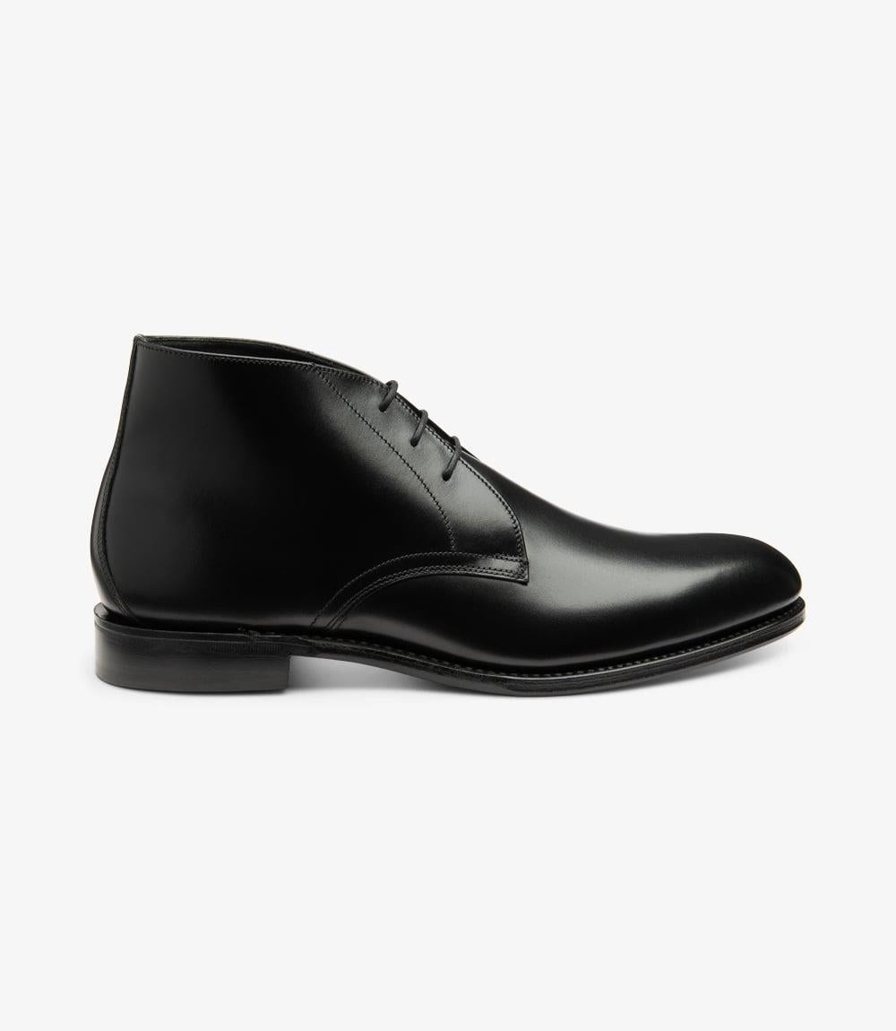 This image showcases the Loake Deangate Black Chukka Boot from the side, highlighting its sleek silhouette and refined design. The boot is crafted from high-quality black leather, featuring a smooth finish that reflects light subtly. The chukka style, characterized by its ankle-height and minimalistic lace-up design, is evident here. The Goodyear welt construction is visible at the sole, emphasizing the boot’s durability and craftsmanship. 