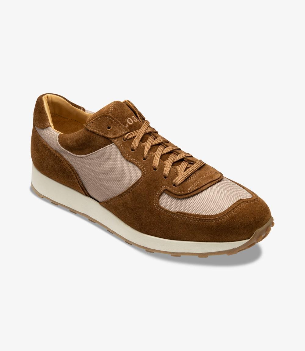 This photo captures one Foster Tan Sneaker from an angle, emphasizing its unique shape and materials. The toe of the sneaker is slightly raised, showcasing the subtle curvature of the sole. The contrast between the suede and canvas is highlighted, with the Loake logo discreetly visible on the side, adding a touch of brand sophistication to the overall look.