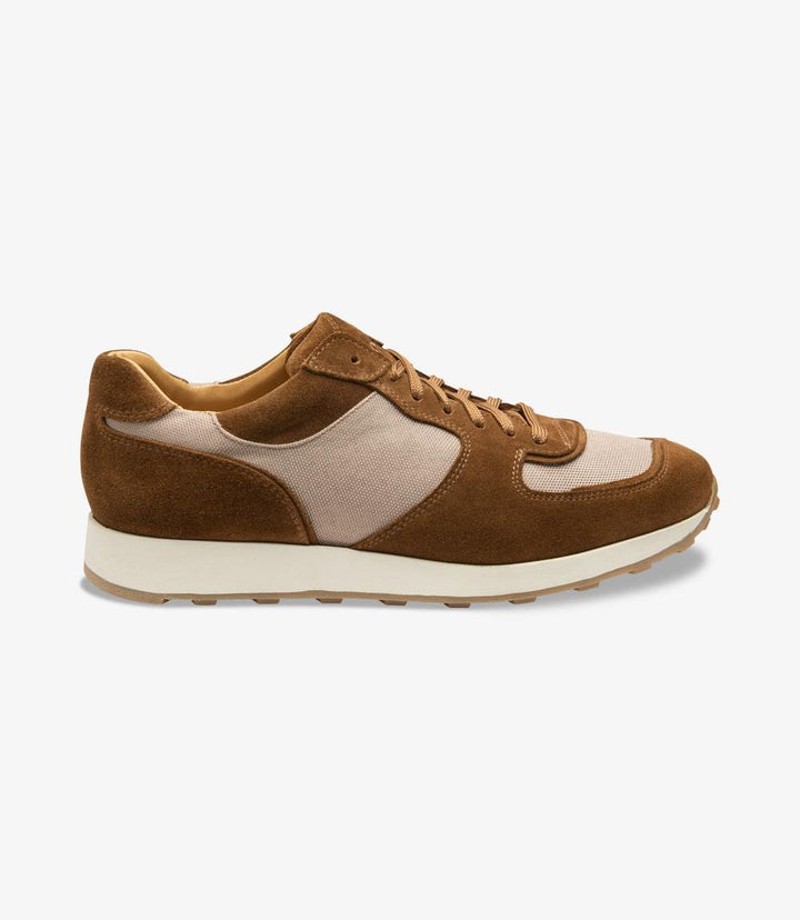 The image showcases the Loake Foster Tan Sneaker from the side, highlighting its sleek silhouette. The rich tan suede and canvas upper blend seamlessly, accentuated by the elegant stitching details. The cemented rubber sole is visible, providing a sturdy foundation for the sneaker, while the classic design conveys both casual style and sophistication.