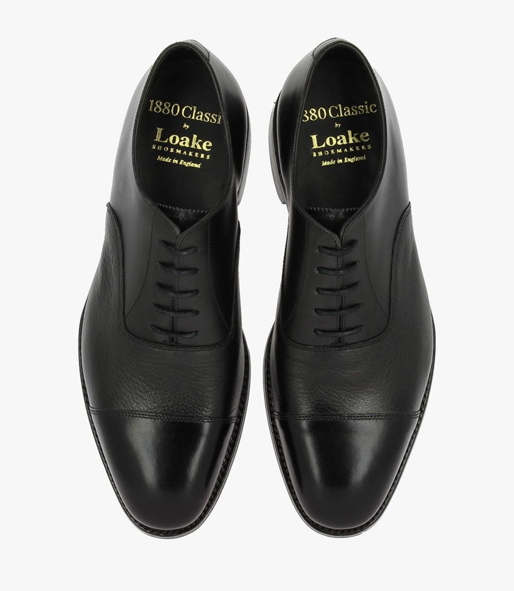 This overhead shot captures the entirety of the Loake Fullerton Black Oxford, presenting its sleek lines and polished toe cap. The symmetrical design of the laces is prominently displayed, reflecting the shoe's classic Oxford aesthetic. The luxurious materials and attention to detail are clear, making it an eye-catching piece for any wardrobe.