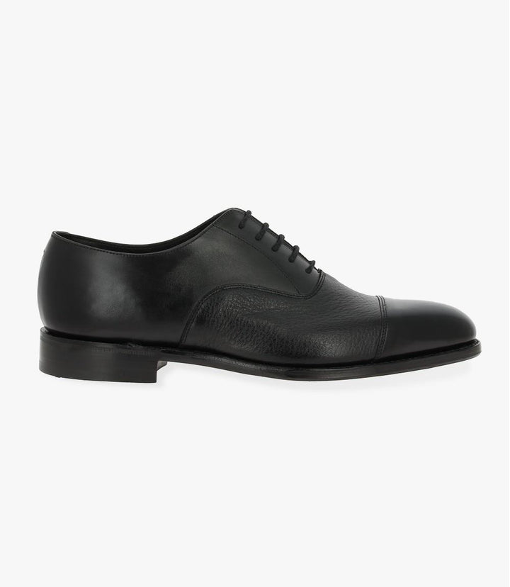 This image showcases the Loake Fullerton Black Oxford Toe Cap from the side, highlighting its elegant silhouette and polished finish. The high-quality European calf leather gleams softly under the light, accentuating the shoe's classic design. The toe cap is distinctly visible, demonstrating the meticulous craftsmanship that defines this premium Oxford shoe.