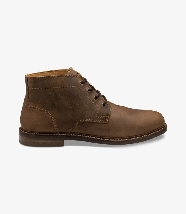 The side view showcases the sleek silhouette of the Loake Gilbert Brown Chukka Boot, highlighting its oiled nubuck leather upper with a rich brown finish. The boot features a clean, minimalist design, accentuated by the subtle stitching that adds depth to its craftsmanship. The cemented rubber sole is clearly visible, emphasizing durability while maintaining a stylish profile.