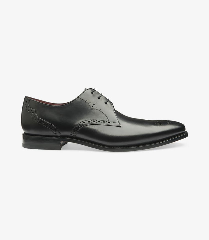 The image captures the Loake Hannibal Black Derby from the side, showcasing its sleek silhouette and elegant lines. The rich, hand-painted calf leather has a polished finish that gleams under light, emphasizing the shoe's sophisticated appeal. The plain front and punched toe detail add subtle texture, while the Goodyear welt construction is visible at the sole, underscoring the shoe's quality craftsmanship.