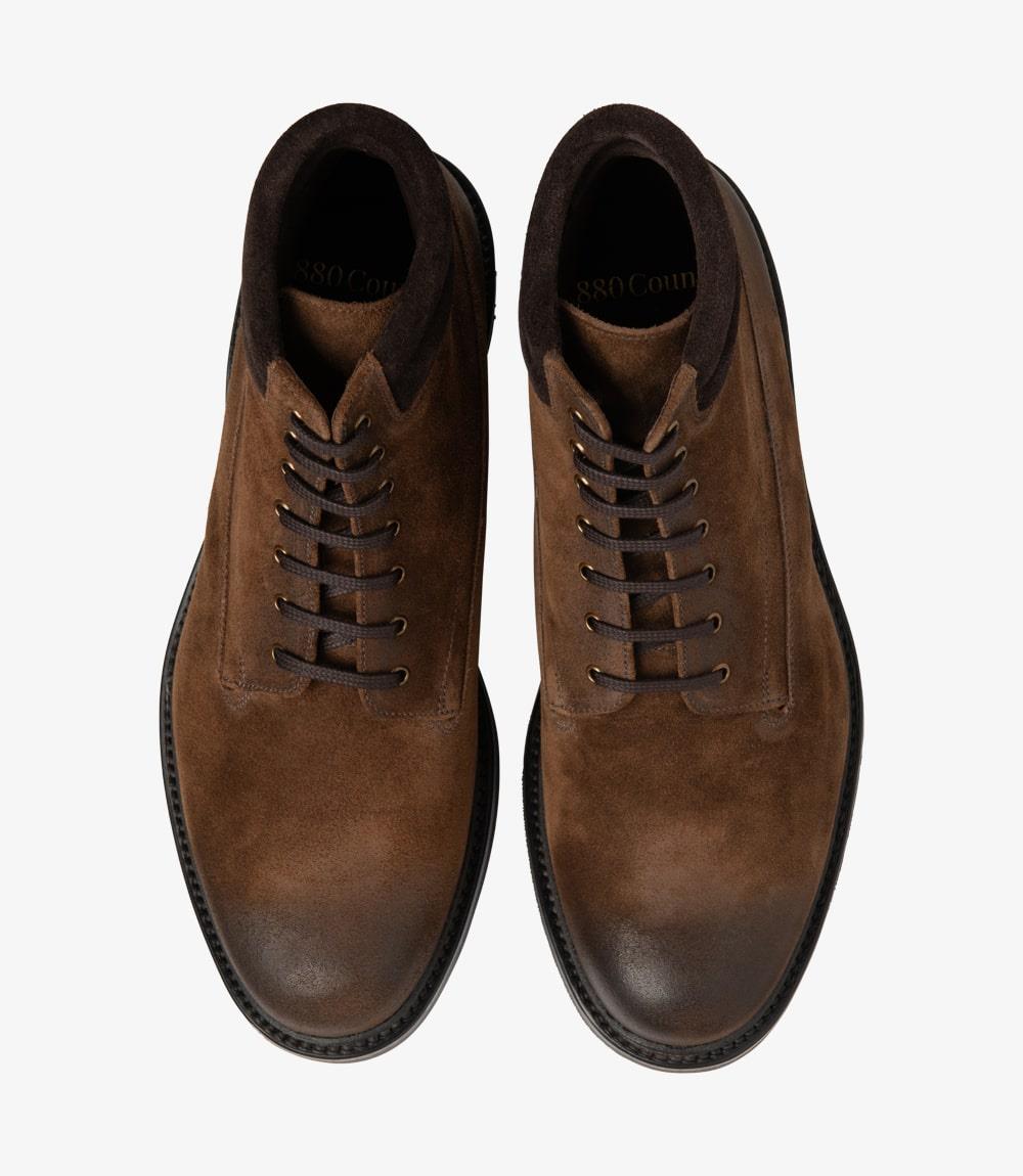 This overhead view of the Loake Kirkby Brown Suede Boot highlights its classic lace-up design. The symmetrical lacing creates a visually appealing pattern, while the rounded toe provides a timeless shape. The padded collar's outline is visible, emphasizing the boot's comfort features. The rich brown suede contrasts beautifully with the robust commando rubber sole, which is designed for optimal grip and durability. This angle showcases the boot's overall craftsmanship and quality.