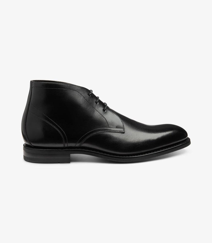 The side view of the Loake Myers Black Chukka Boot highlights its sleek silhouette and elegant design. The rich, hand-painted calf leather presents a deep black finish, accentuated by the neat stitching that outlines the 3-eyelet lacing system. The ankle height is modest, offering a refined look while maintaining a modern aesthetic. The Goodyear welted shadow rubber sole is visible at the base, providing a sturdy foundation that blends seamlessly with the overall sleekness of the boot.