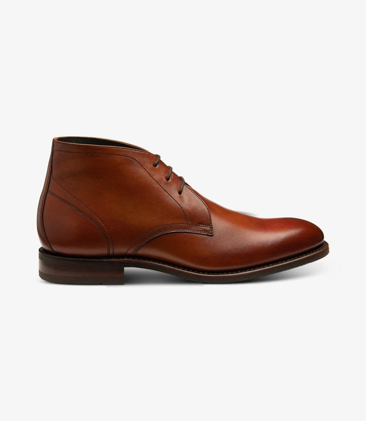 The Loake Myers Tan Chukka Boot presents a classic silhouette with its smooth, hand-patina calf leather in a warm tan hue. The side profile showcases the elegant 3-eyelet lacing system and neatly stitched seams that enhance its refined look. The Goodyear welted shadow rubber sole is visible at the base, providing a sturdy foundation while adding a touch of modernity. The slightly rounded toe and low ankle height contribute to a versatile and stylish appearance suitable for both casual and smart-casual wear.