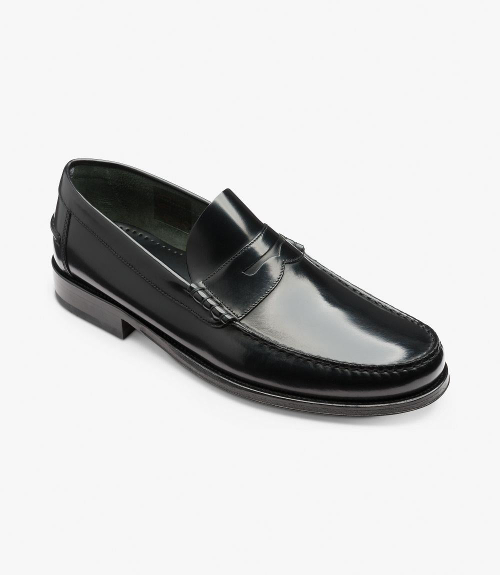 In this angled view, the Loake Princeton Black Loafer presents a dynamic perspective, emphasizing its craftsmanship and design features. The polished black leather wraps smoothly around the shoe, with the beef-roll detail accentuated at the forefront. The slight elevation of the flexible leather sole is visible, demonstrating the shoe's practicality and comfort. This angle also highlights the rounded toe shape and the elegant lines that define the loafer.