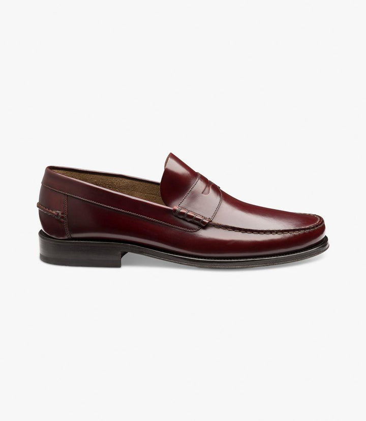 The side view of the Loake Princeton Burgundy Loafer showcases its elegant silhouette and polished finish. The rich burgundy leather gleams under the light, highlighting the shoe's luxurious texture. The rounded toe complements the beef-roll design, adding a touch of sophistication. The flexible leather sole is subtly visible at the base, indicating both style and comfort. This perspective emphasizes the clean lines and refined shape of the loafer, making it a versatile choice for various occasions.