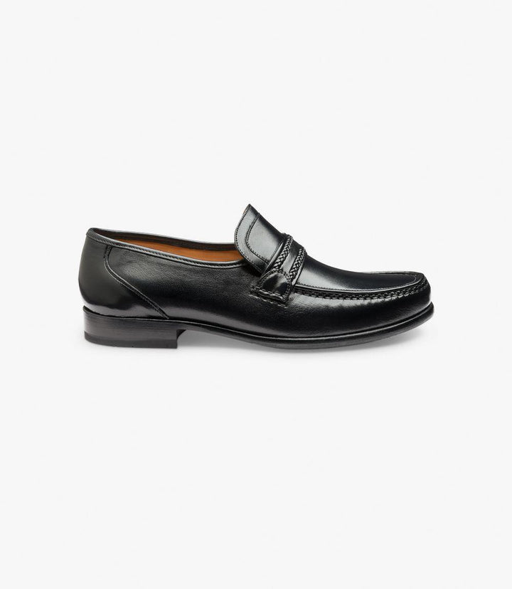 The side view showcases the Loake Rome Black Loafer in its entirety, highlighting its smooth, premium black Nappa leather finish. The classic rounded toe and the extra-wide fit provide a subtle, elegant curve, while the moccasin stitching details add character to the design. The flexible leather sole is visible along the edge, emphasizing quality craftsmanship.