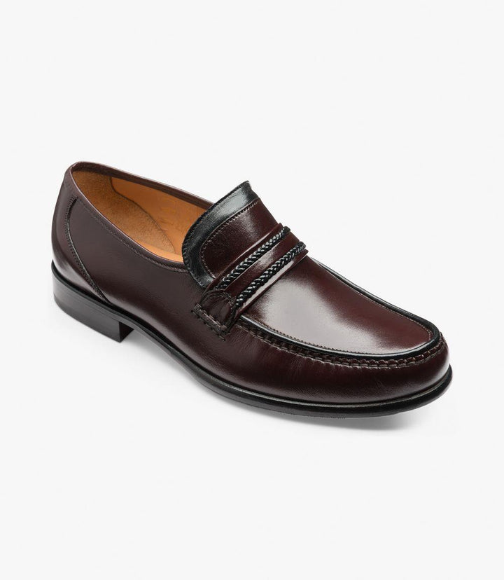 The shoe is positioned at an angle, showcasing both the rounded toe and the low-profile heel. The polished burgundy leather shines under the light, with detailed stitching visible along the vamp. This angle also reveals the loafer's sleek silhouette and extra-wide GX fit, designed for superior comfort.